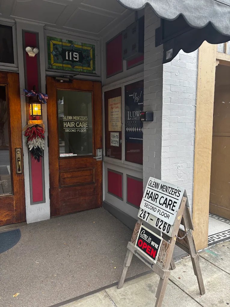 The street entrance at 119 South Main Street: a wooden door lettered Glenn Mentzer's Hair Care, Second Floor, with a sidewalk sign that says Come in, we're open.