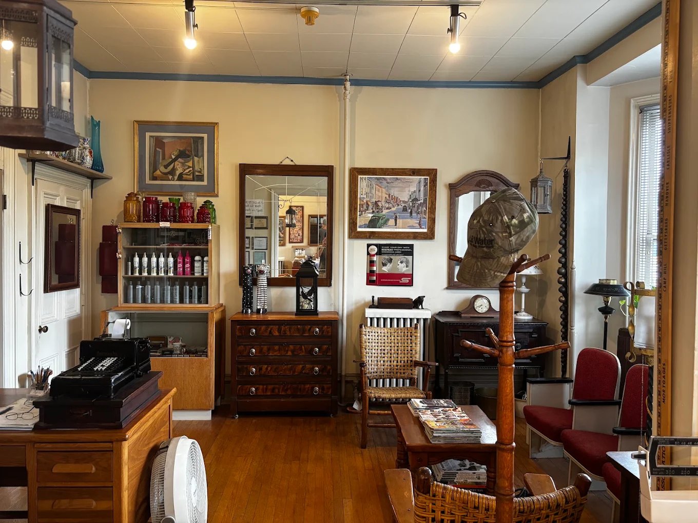 The waiting area: an antique adding machine on a wooden desk, a chest of drawers, framed mirrors and pictures, and red waiting chairs.